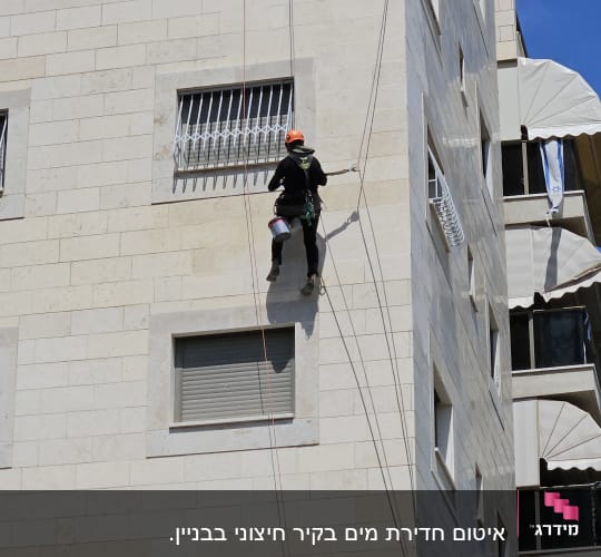 אדם עם קסדה מטפס על קיר בניין בעזרת חבלים